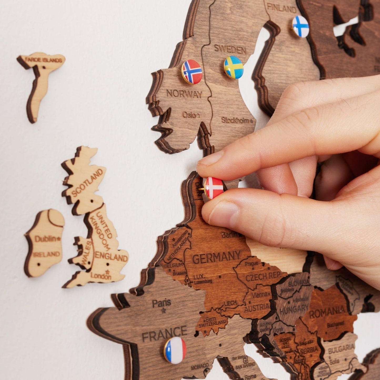 Världskarta i trä med flaggor: Planera och minns dina resor. Dekorativ trä-världskarta med pins som markerar besökta länder i Europa, inklusive Sverige, Tyskland och Storbritannien. Perfekt väggdekoration för resefantaster."